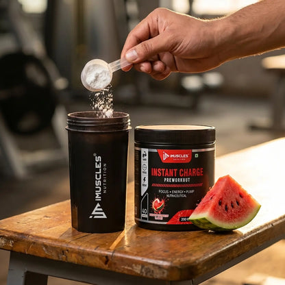 Close-up action shot of a person pouring a compact scoop of ultra-pure white pre-workout powder into a matte black iMUSCLES NUTRITION shaker bottle. The setup rests on a rustic wooden gym bench next to a 200g container of Instant Charge Pre-Workout and a fresh slice of watermelon, capturing a premium, cinematic gym atmosphere.