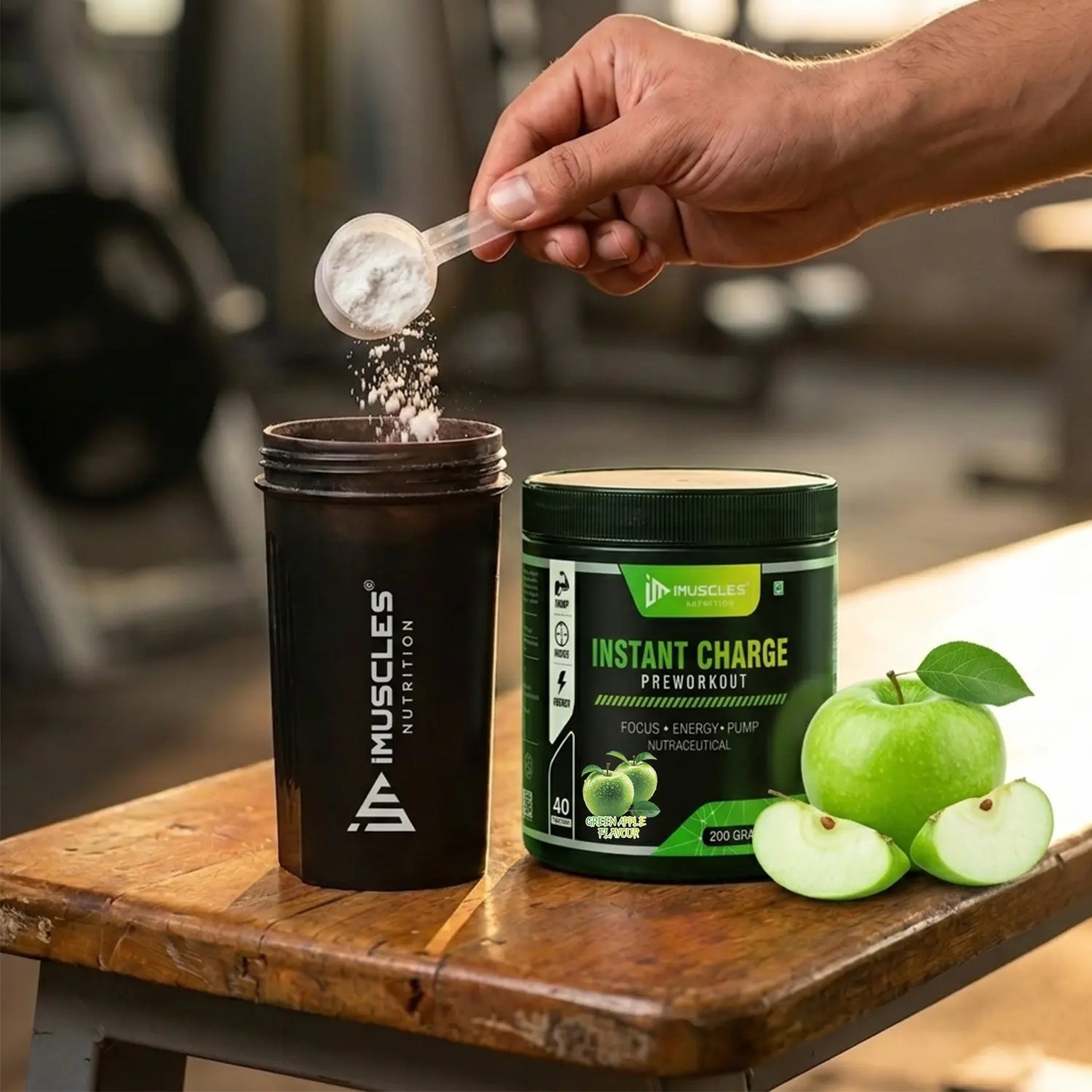 An action commercial photograph labeled "Green Apple 7.jpg" showing a man's hand pouring a scoop of pre-workout powder into an iMuscles Nutrition shaker bottle. The "INSTANT CHARGE" Green Apple flavour supplement jar sits next to it on a rustic wooden gym bench, garnished with a whole green apple and fresh apple slices.