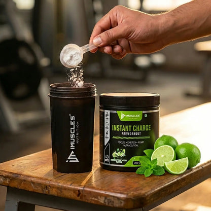 An action commercial photograph labeled "Tropical Twist Mojito 7.jpg" showing a man's hand pouring a scoop of pre-workout powder into an iMuscles Nutrition shaker bottle. The "INSTANT CHARGE" supplement jar sits next to it on a rustic wooden gym bench, garnished with fresh whole limes, lime slices, and mint leaves.
